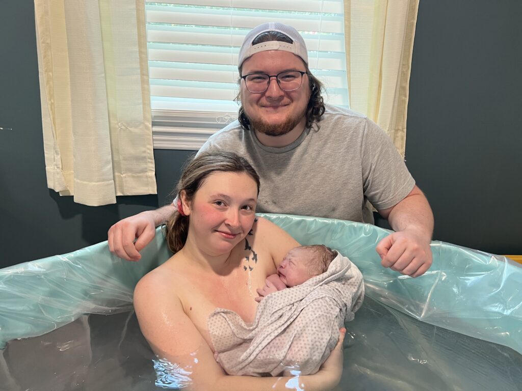 me and my husband posing with our newborn son in the birth pool